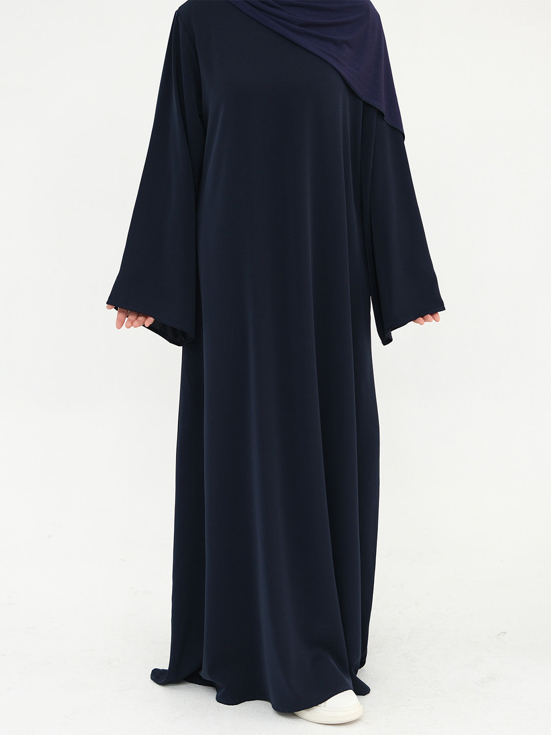 A person wearing a long navy abaya dress with wide sleeves and a matching navy hijab, shown from the back against a plain white studio background.