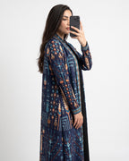 A woman takes a mirror selfie wearing a long-sleeved navy blue open-front cardigan with a detailed geometric and tribal pattern in orange, beige, and teal, set against a plain light gray background.