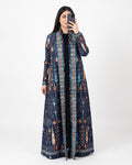 A woman takes a mirror selfie wearing a long navy blue open-front kaftan dress with an intricate multicolor geometric and tribal pattern in blue, orange, and beige, over a black top, against a plain white studio background.