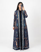 A woman takes a mirror selfie wearing a long navy blue open-front kaftan dress with an intricate multicolor geometric and tribal pattern in blue, orange, and beige, over a black top, against a plain white studio background.