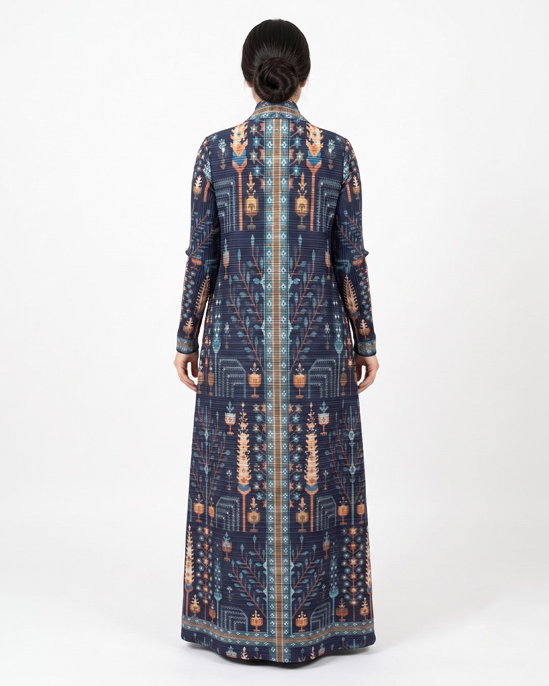 A woman viewed from the back wearing a long-sleeved navy blue maxi dress with an intricate geometric and tribal pattern in beige, orange, and light blue, set against a plain white studio background.