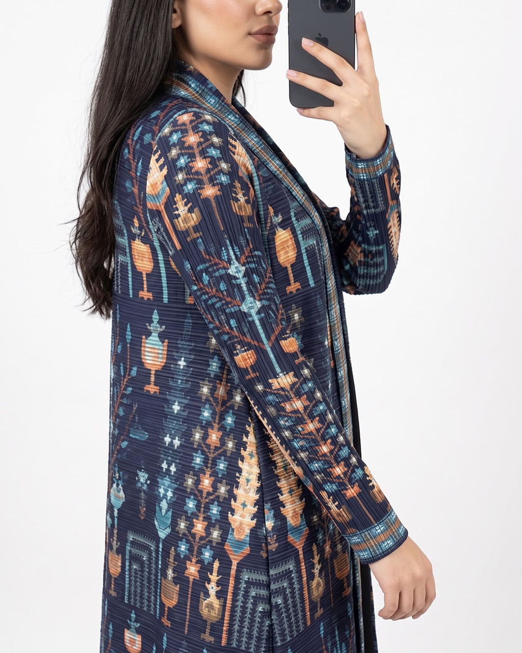 A woman takes a mirror selfie wearing a long-sleeved open-front cardigan with a detailed geometric and tribal-inspired pattern in navy blue, orange, and light blue.