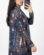 A woman takes a mirror selfie wearing a long-sleeved open-front cardigan with a detailed geometric and tribal-inspired pattern in navy blue, orange, and light blue.