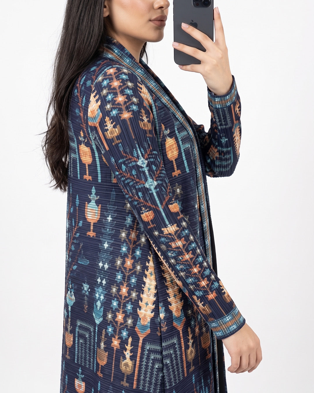 A woman takes a mirror selfie wearing a long-sleeved open-front cardigan with a detailed geometric and tribal-inspired pattern in navy blue, orange, and light blue.