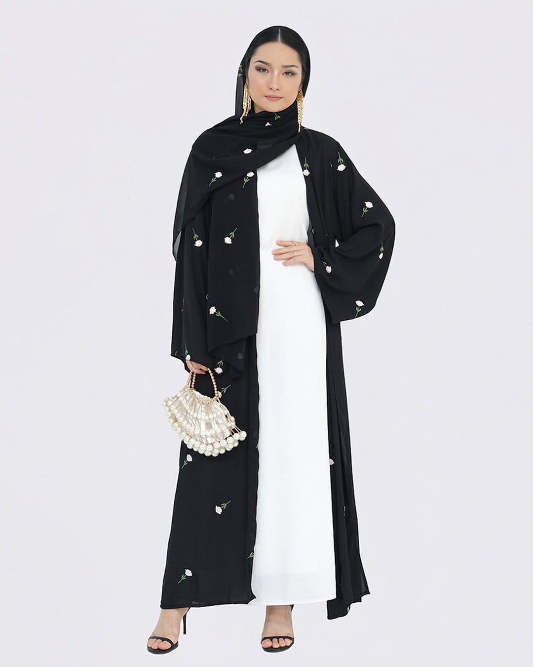 Woman wearing a black abaya with pearl embellishments on a white background