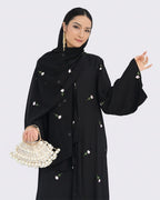 Woman wearing a black abaya with floral embroidery on a white background
