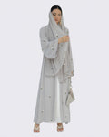 Woman wearing a light gray embroidered dress and hijab on a white background