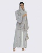 Woman wearing a light gray embroidered dress and hijab on a white background