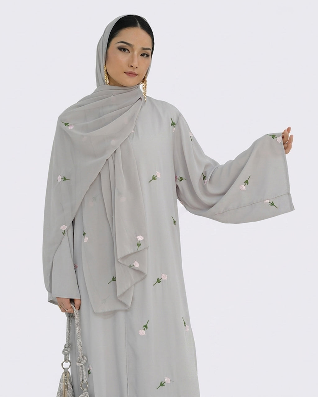 Woman wearing a light gray abaya with floral embroidery on a white background