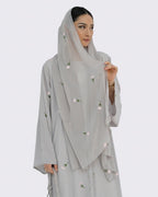 Woman wearing a light gray outfit with floral embroidery on a white background