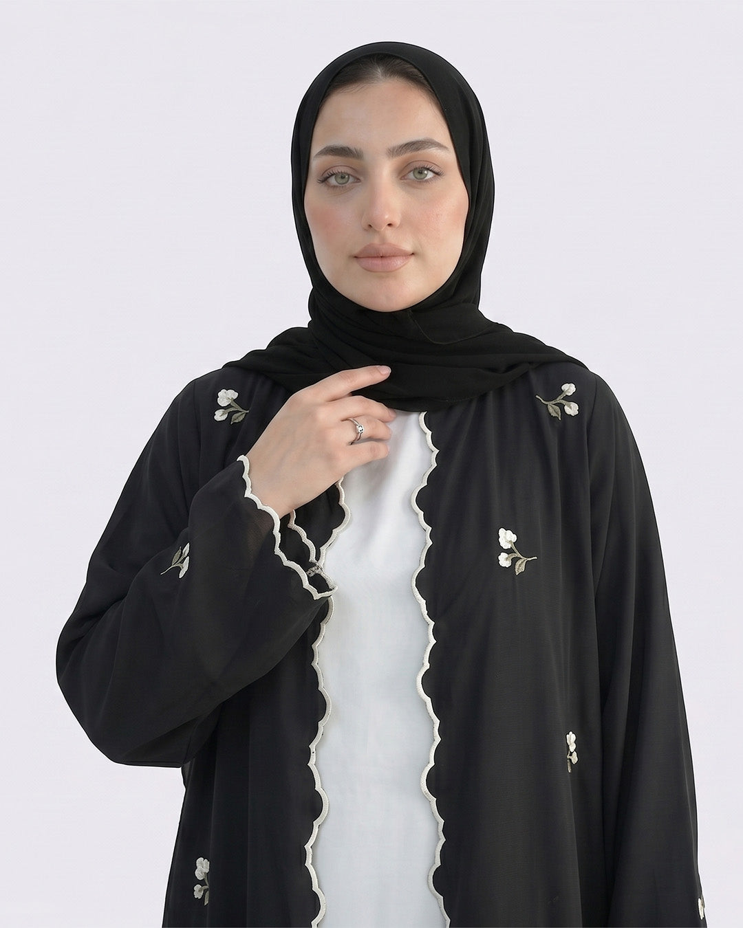 Woman wearing a black abaya with white embroidery on a white background