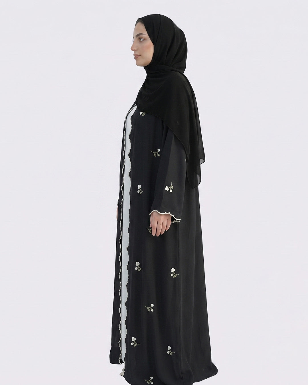 Woman wearing a black abaya with white embellishments on a white background