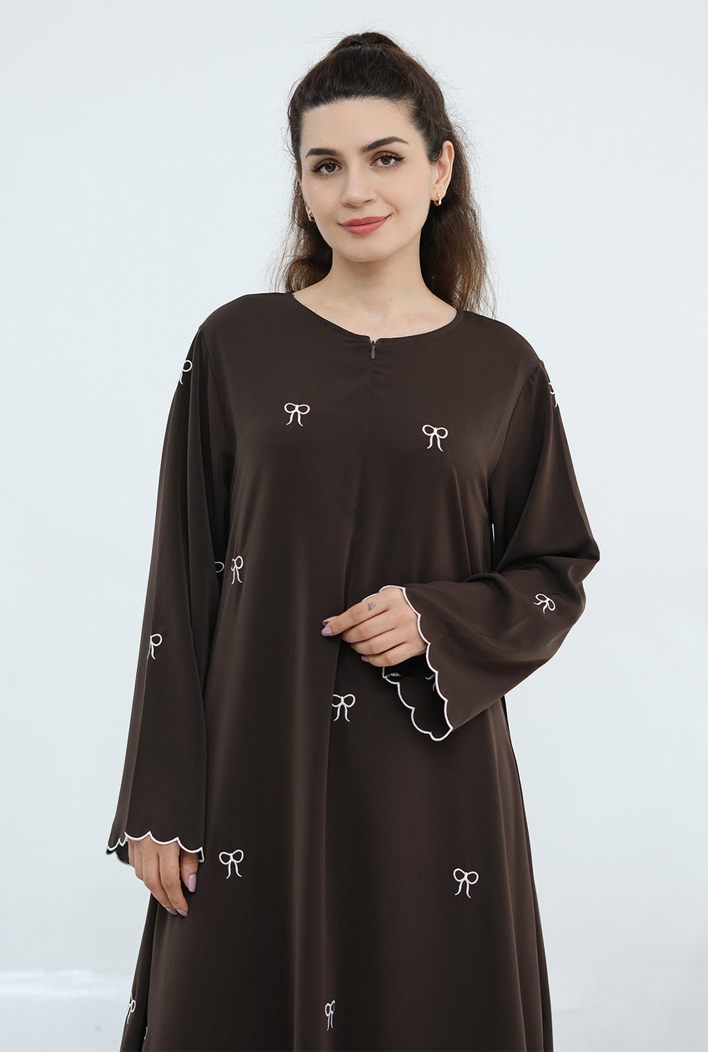 Woman wearing a brown dress with white embroidery on a white background