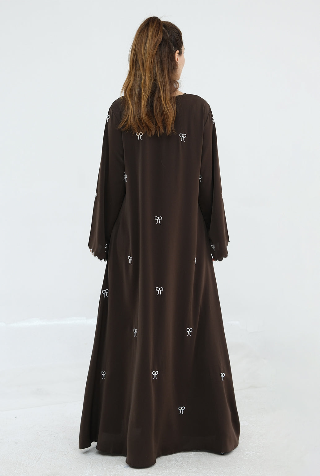 Woman wearing a long brown dress with white patterns on a white background