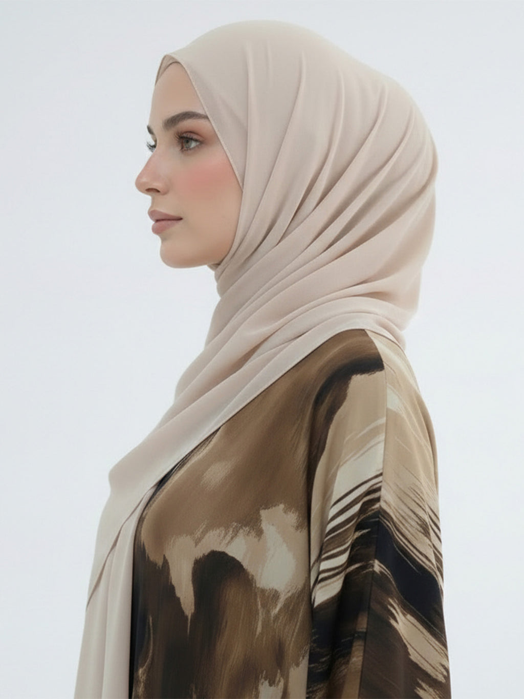 A woman in profile wearing a light beige hijab and a brown abstract-printed blouse against a plain light gray background.