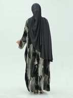 A woman shown from the back wearing a long black hijab and a long-sleeved abaya with a black, gray, and white abstract marbled pattern, set against a plain light gray studio background.