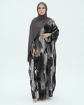 A woman wearing a long-sleeved abaya dress with a black and gray abstract watercolor pattern, paired with a solid dark gray hijab, standing against a light gray studio background.