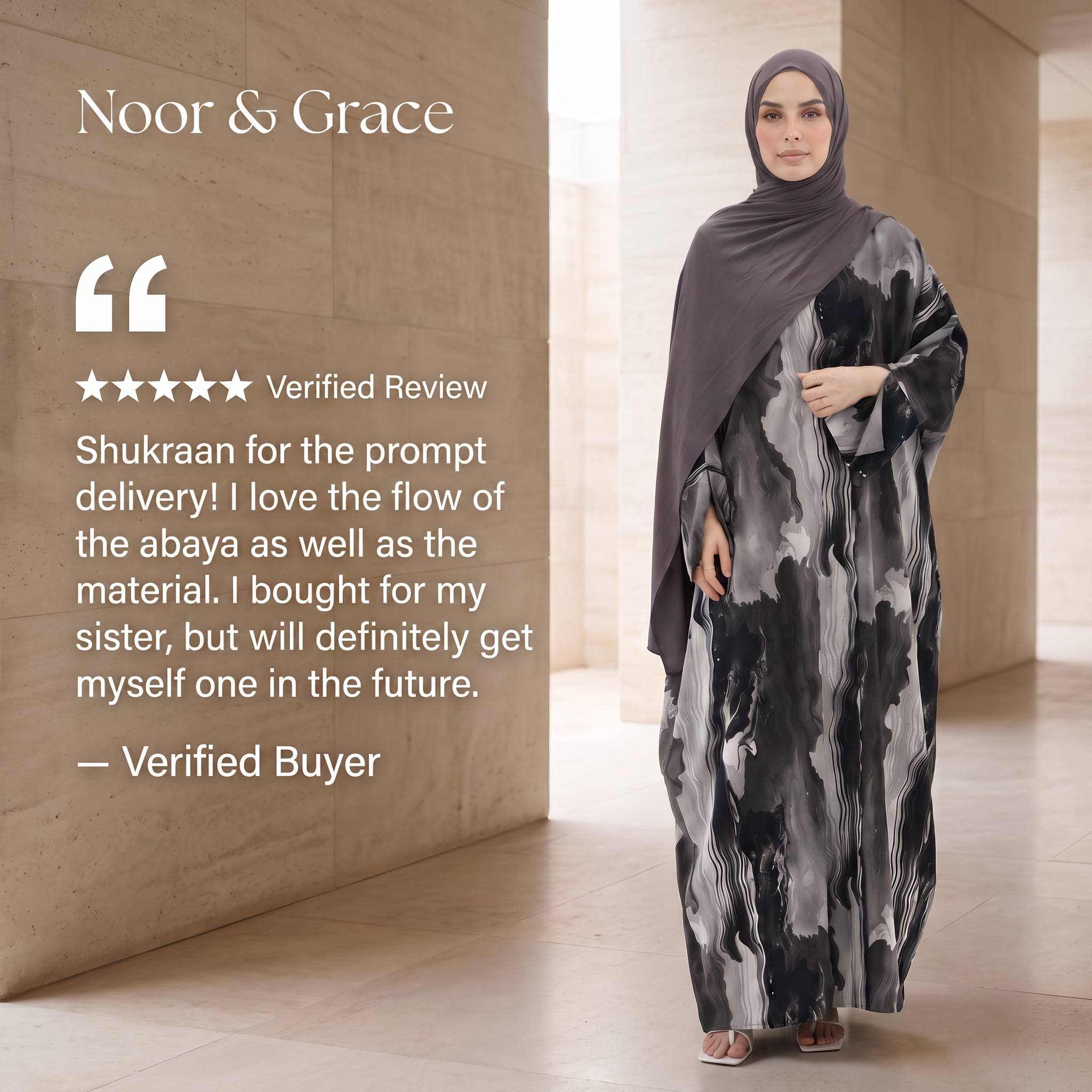 A woman wearing a Noor & Grace abaya and hijab stands in a modern interior with beige stone walls. The abaya is floor-length with an abstract black, gray, and white brushstroke pattern, and the hijab is a solid dark gray.