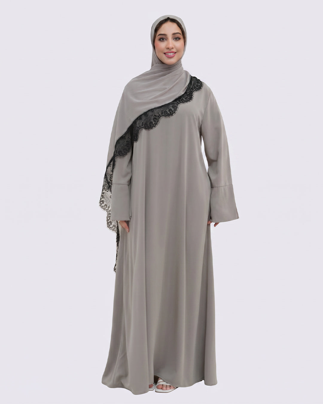 Woman wearing a gray abaya with black lace details on a white background