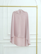 A dusty pink high-neck draped blouse with long flowing sleeves, hanging on a gold clothing rack against a white paneled wall.