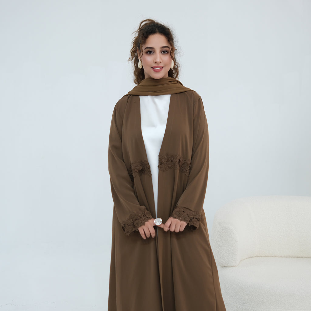 A woman modeling a long brown abaya with lace trim on the cuffs and front, worn over a white top and paired with a matching brown scarf, set against a clean white studio background.