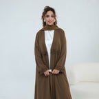 A woman modeling a long brown abaya with lace trim on the cuffs and front, worn over a white top and paired with a matching brown scarf, set against a clean white studio background.