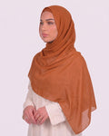 Model wearing a lightweight, pumpkin chiffon hijab wrapped elegantly over a beige long-sleeved dress.