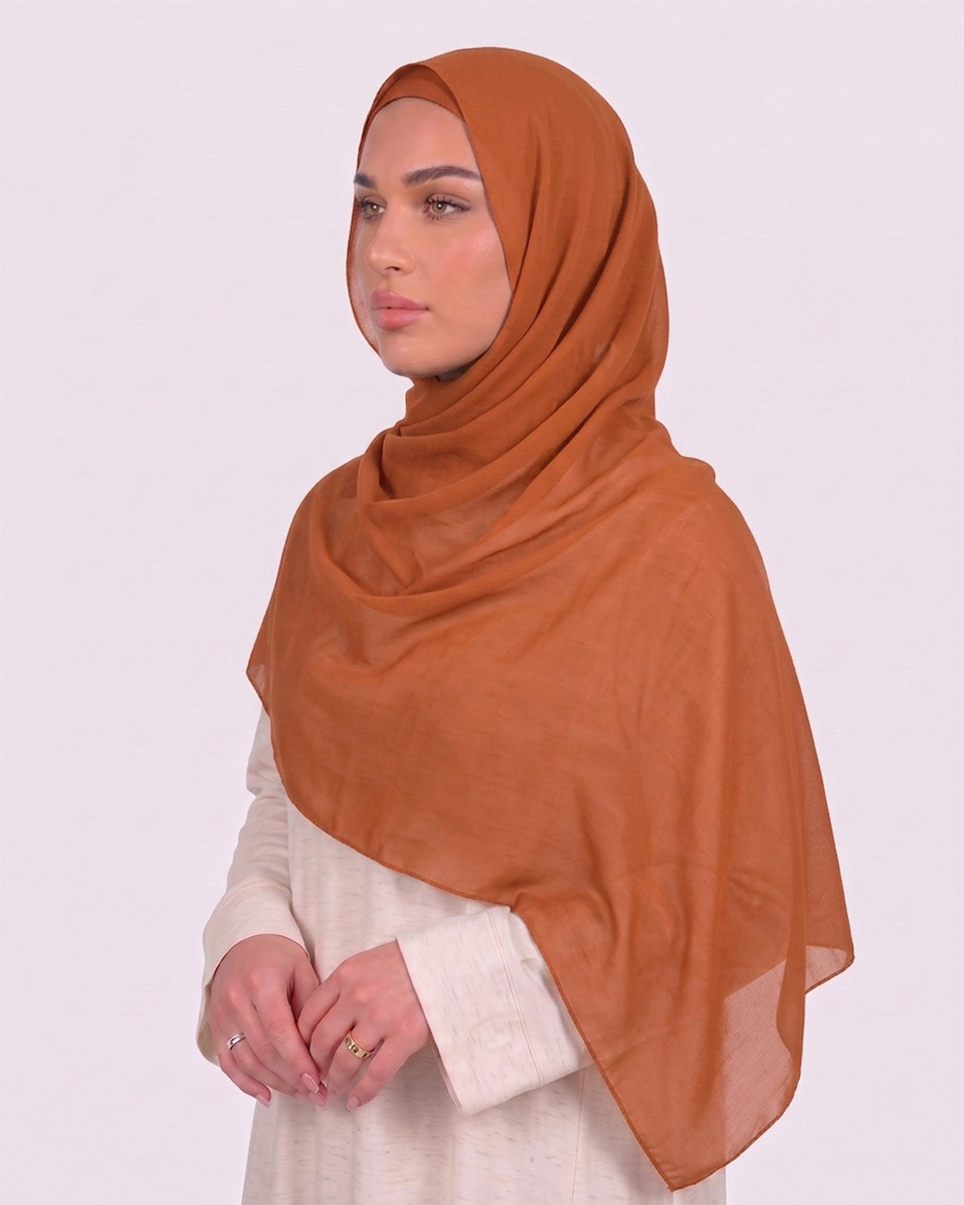 Model wearing a lightweight, pumpkin chiffon hijab wrapped elegantly over a beige long-sleeved dress.
