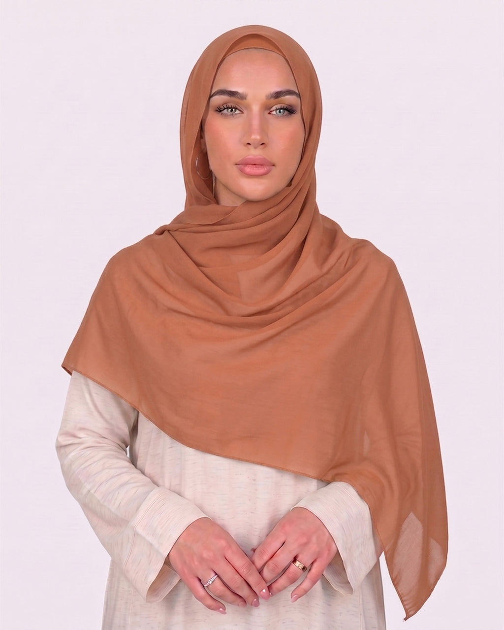 Model wearing a lightweight, pumpkin chiffon hijab wrapped elegantly over a beige long-sleeved dress.