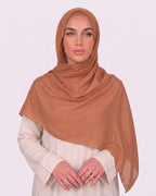 Model wearing a lightweight, pumpkin chiffon hijab wrapped elegantly over a beige long-sleeved dress.