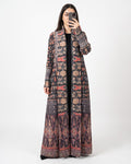 A woman takes a mirror selfie wearing a long, open-front maxi dress with an intricate multicolor geometric and tribal pattern in shades of brown, beige, red, and black.
