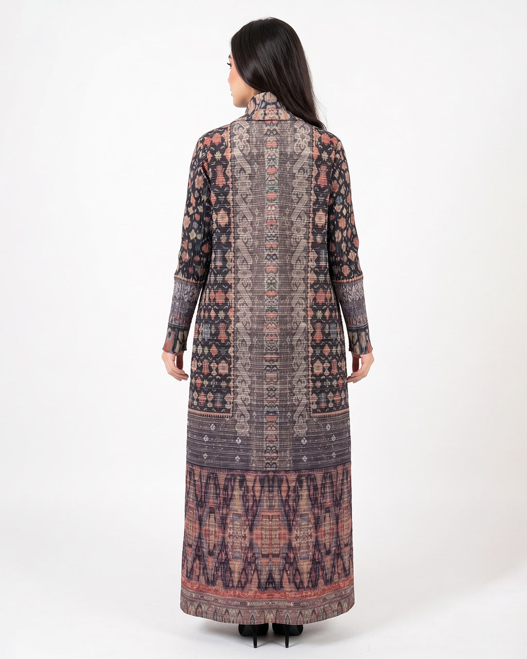 A woman viewed from the back wearing a long-sleeved, high-neck maxi dress with an intricate multicolor geometric and tribal pattern in shades of brown, pink, and purple, set against a plain white studio background.