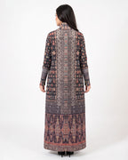 A woman viewed from the back wearing a long-sleeved, high-neck maxi dress with an intricate multicolor geometric and tribal pattern in shades of brown, pink, and purple, set against a plain white studio background.