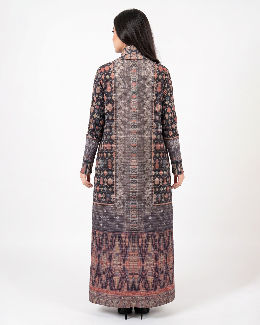 A woman viewed from the back wearing a long-sleeved, high-neck maxi dress with an intricate multicolor geometric and tribal pattern in shades of brown, pink, and purple, set against a plain white studio background.