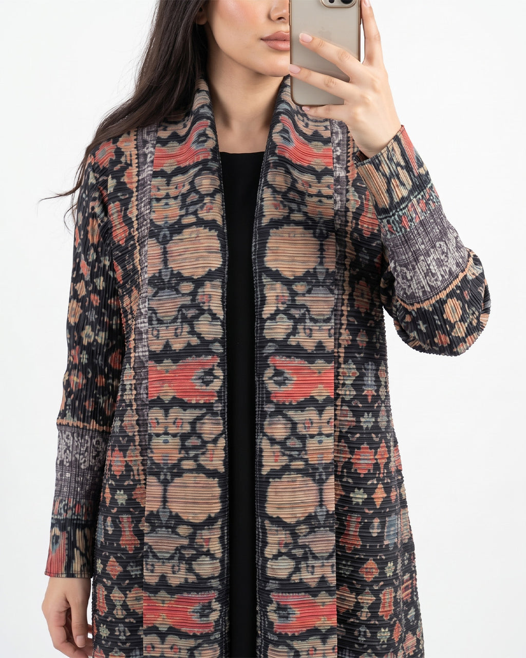 A woman takes a mirror selfie showing off a long-sleeve open-front cardigan with a complex geometric and tribal-inspired pattern in black, beige, and coral red.
