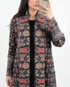 A woman takes a mirror selfie showing off a long-sleeve open-front cardigan with a complex geometric and tribal-inspired pattern in black, beige, and coral red.