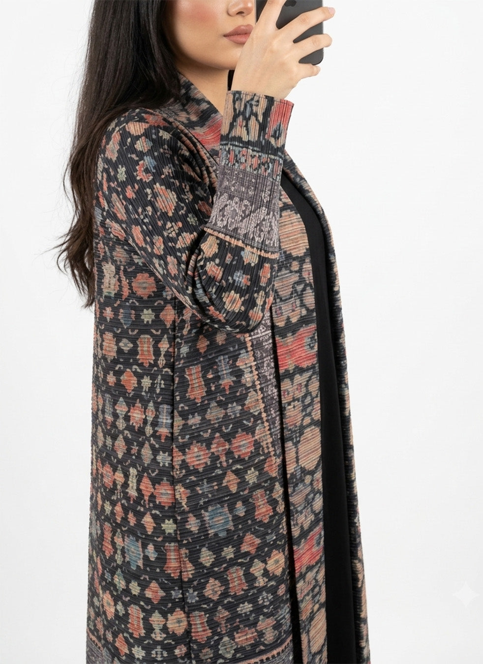 A woman wearing a long open-front cardigan with a multicolor geometric and tribal-inspired pattern on a black base, shown in a side profile against a plain white background.