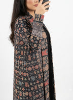 A woman wearing a long open-front cardigan with a multicolor geometric and tribal-inspired pattern on a black base, shown in a side profile against a plain white background.