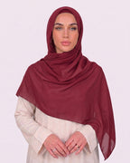 Model wearing a lightweight, rose red chiffon hijab wrapped elegantly over a beige long-sleeved dress.