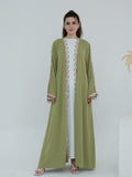 A woman modeling a long olive green abaya dress with pink and green embroidered patterns along the front opening and cuffs, worn over a white inner dress.