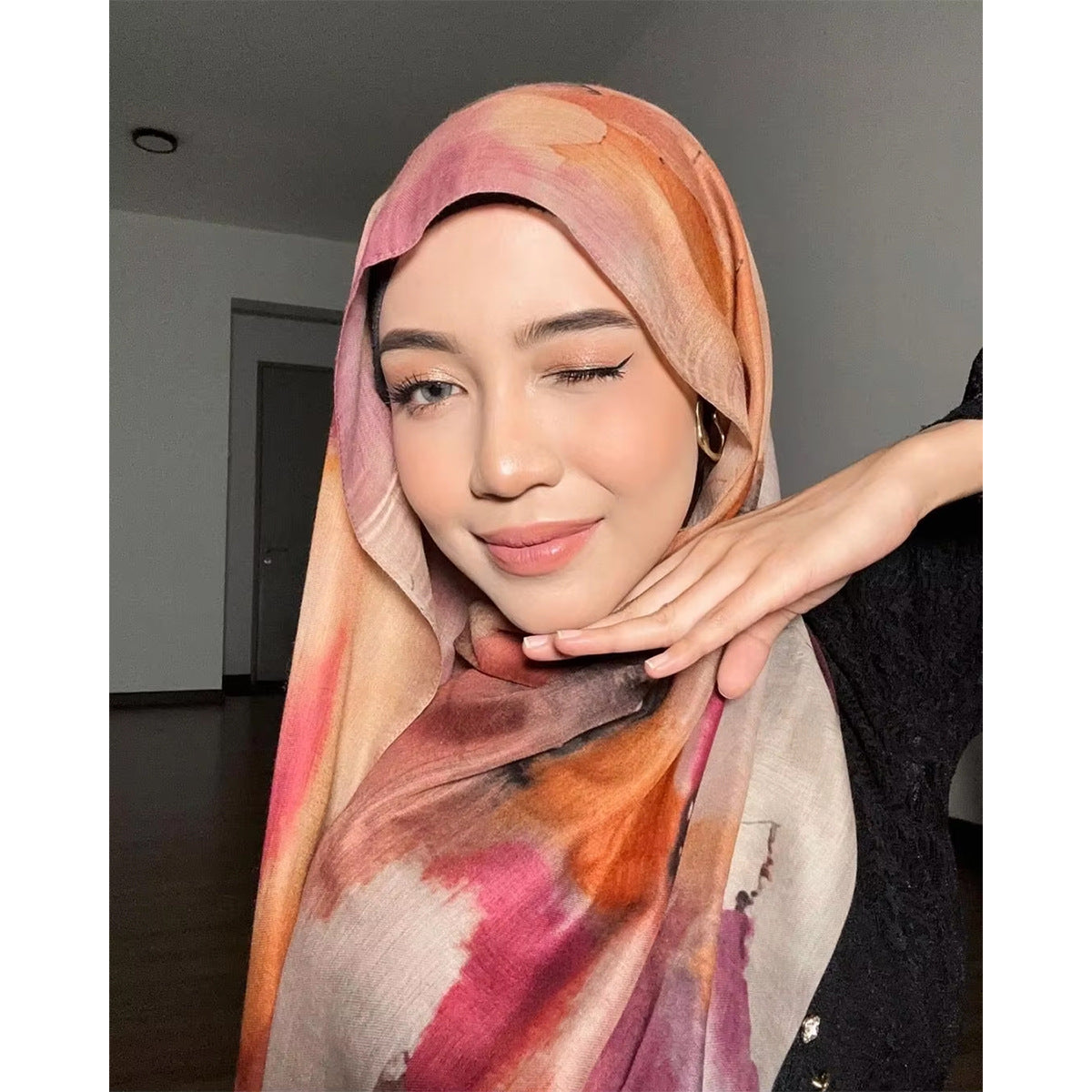 Woman wearing a colorful hijab with another hand adjusting it indoors.