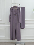 A two-piece women's outfit in a dusty lavender-purple color, consisting of a long-sleeve button-front coat with a collar and matching wide-leg trousers, displayed on a metal clothing rack against a white paneled wall.