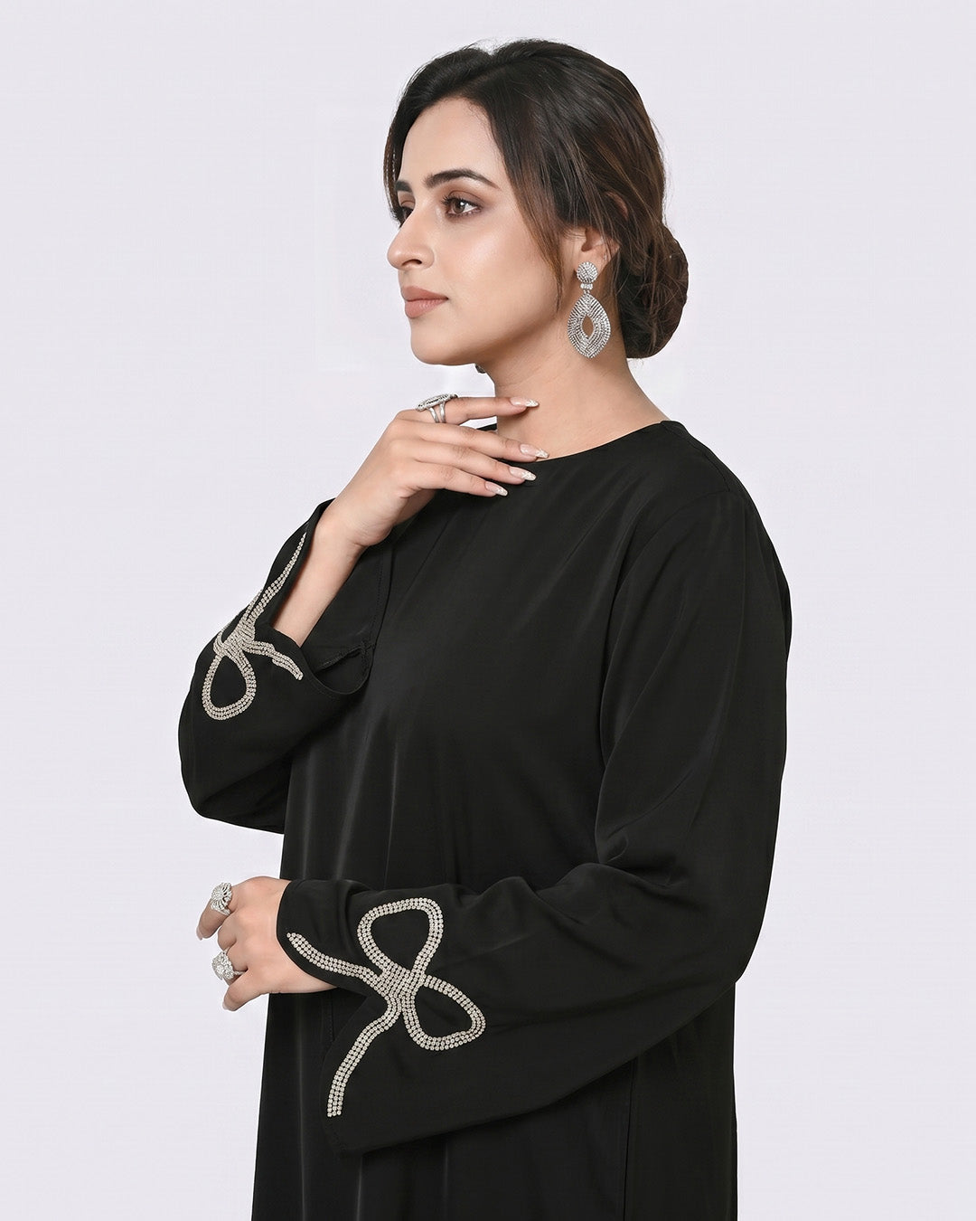 Woman wearing a black abaya with silver embroidery on a white background