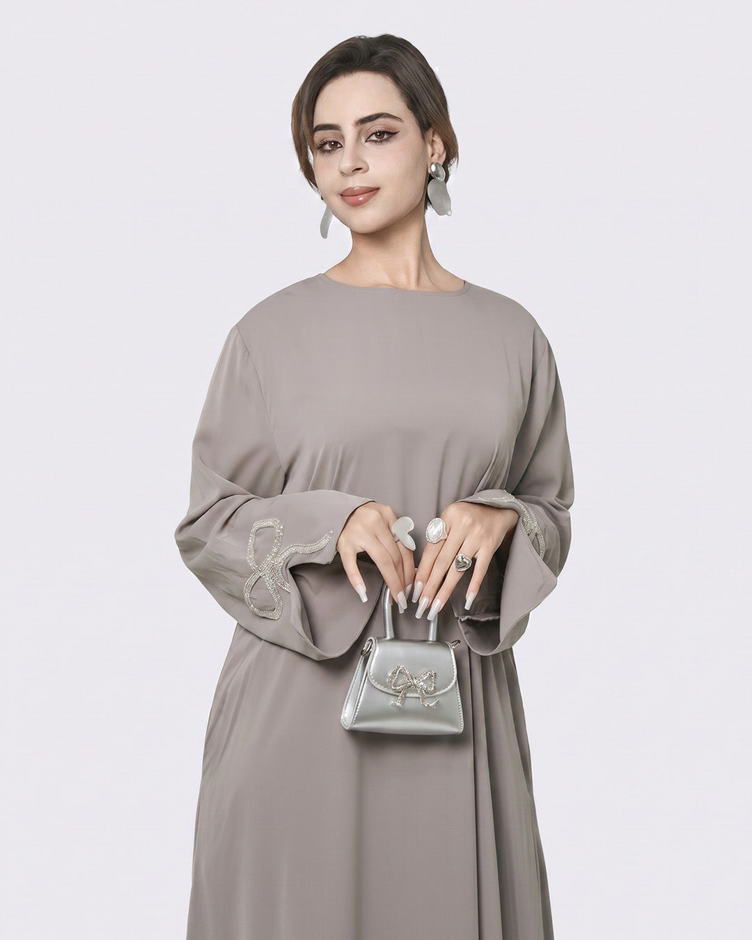 Woman wearing a gray dress holding a silver handbag against a white background