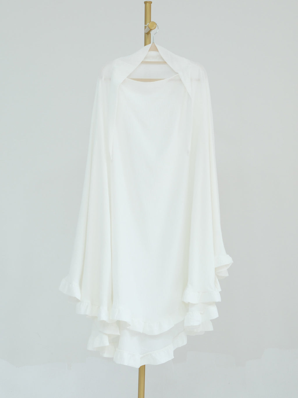 A white long-sleeve blouse with a high-low ruffled hem, displayed on a hanger against a light gray background.