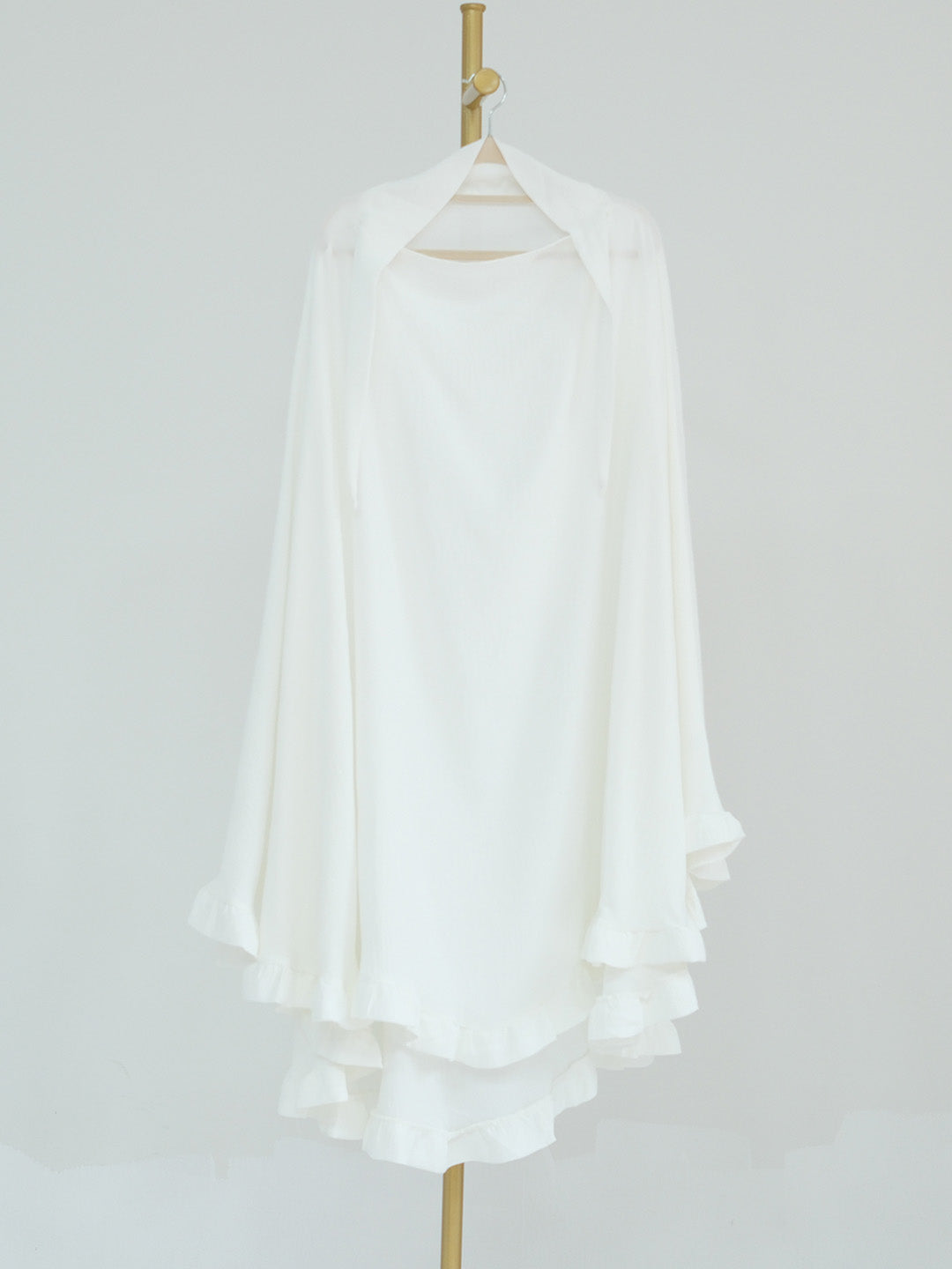 A white long-sleeve blouse with a high-low ruffled hem, displayed on a hanger against a light gray background.