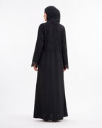 A woman wearing a long black abaya with lace trim on the cuffs and a matching black hijab, shown from the back against a plain white studio background.
