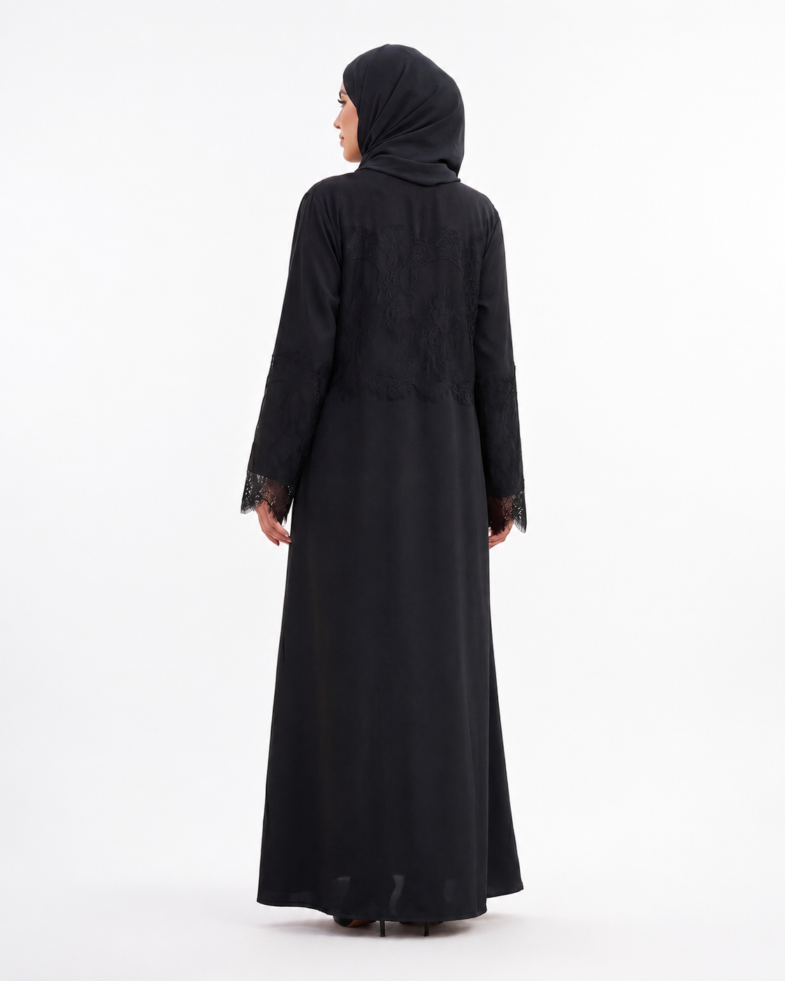 A woman wearing a long black abaya with lace trim on the cuffs and a matching black hijab, shown from the back against a plain white studio background.
