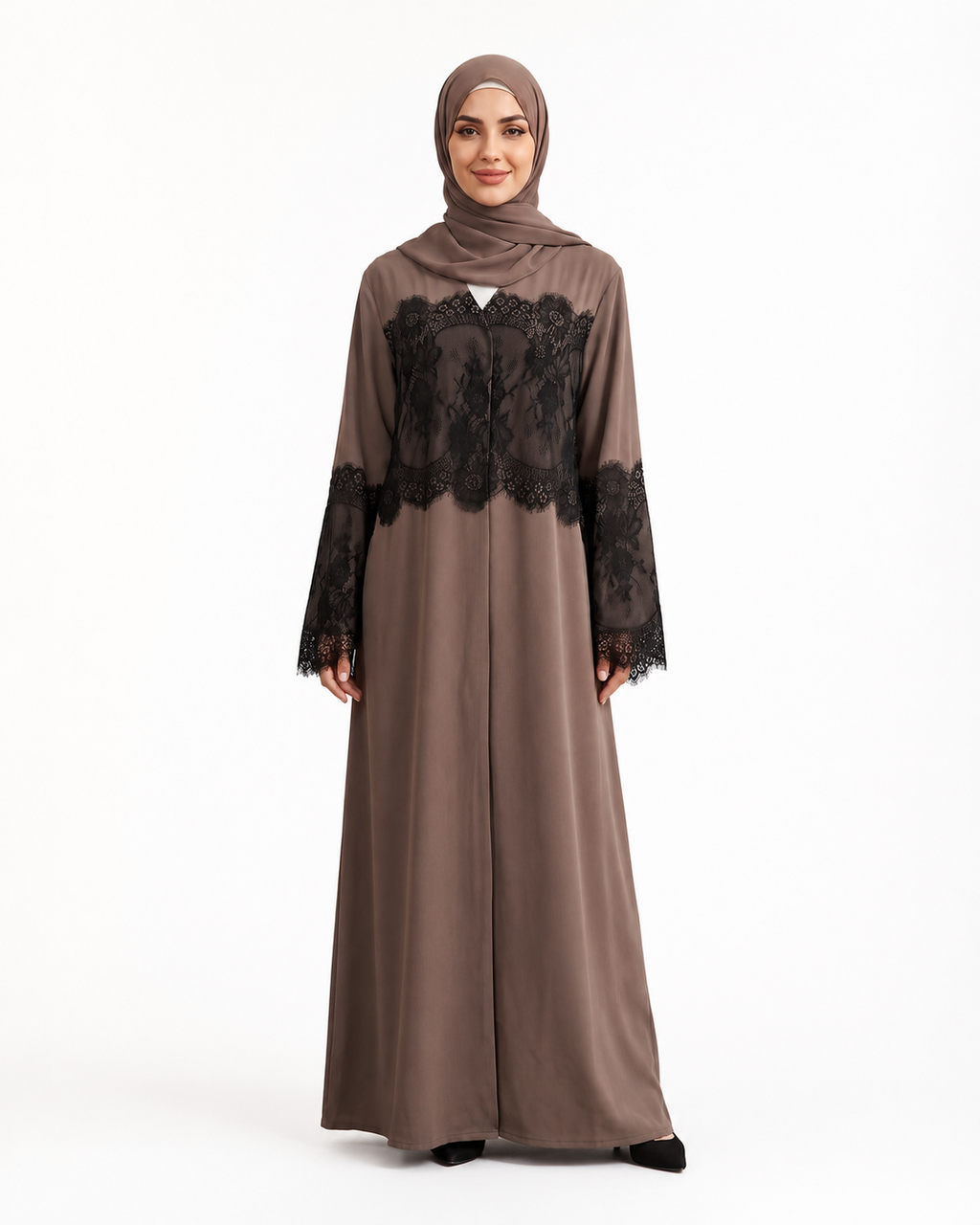 A woman modeling a taupe-brown long abaya dress with black lace panels on the chest and sleeves, paired with a matching hijab, against a plain white studio background.