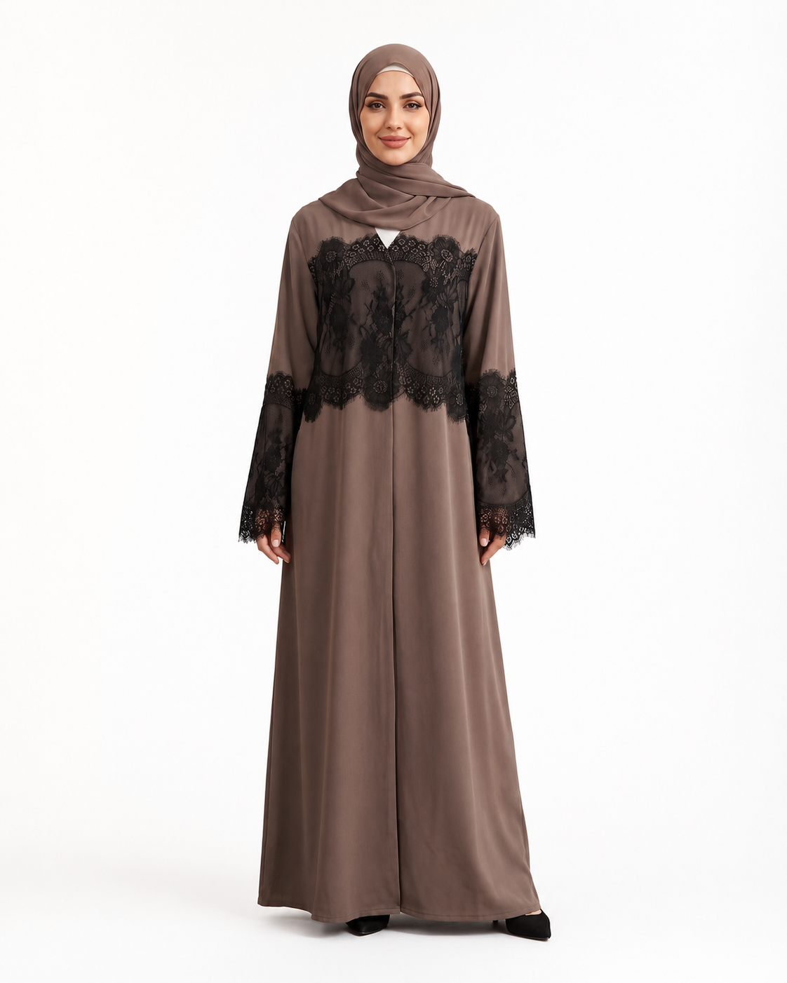 A woman modeling a taupe-brown long abaya dress with black lace panels on the chest and sleeves, paired with a matching hijab, against a plain white studio background.